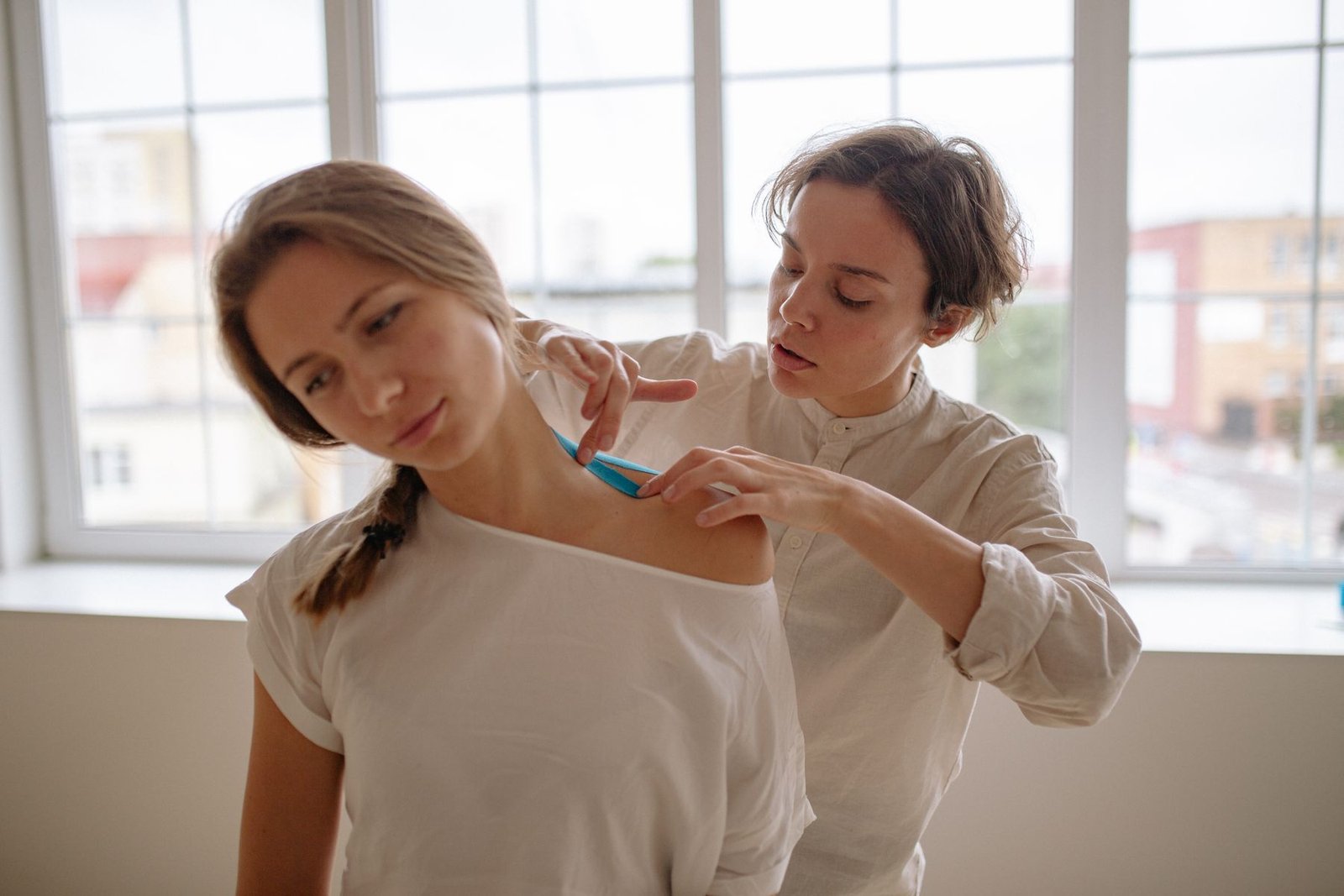 Physiotherapist applying kinesiology tape to a client's shoulder, illustrating whether kinesiology tape actually works