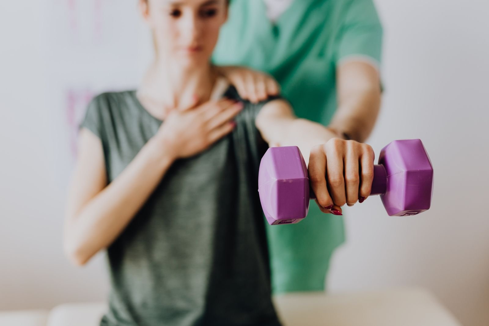 A therapist guiding a patient through a light dumbbell exercise, part of progressive loading for bicep tendonitis elbow pain.