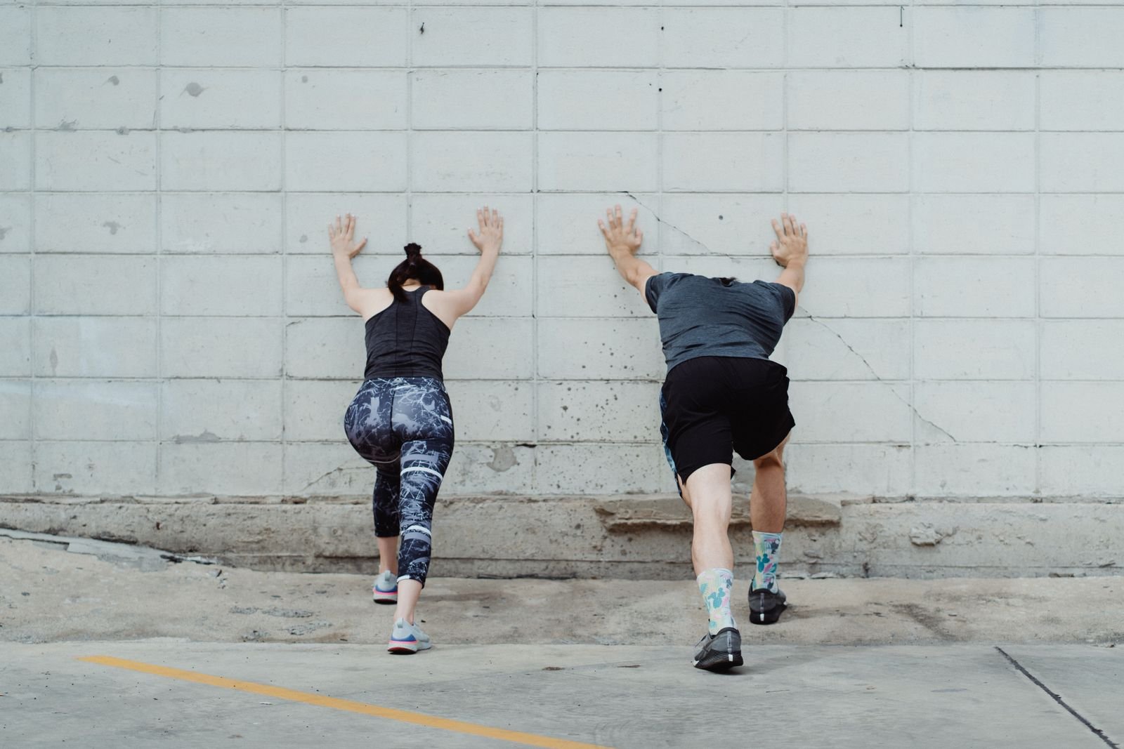 Two runners doing wall calf stretches seen from behind, the kind of shin splints stretches pictures that make heel and foot alignment easy to check.