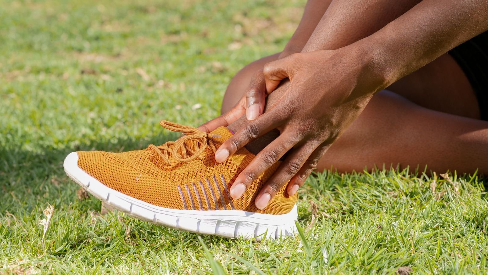 A person holding a sore ankle, a reminder to check for warning signs when learning how to tape a sprained ankle kinesiology style.