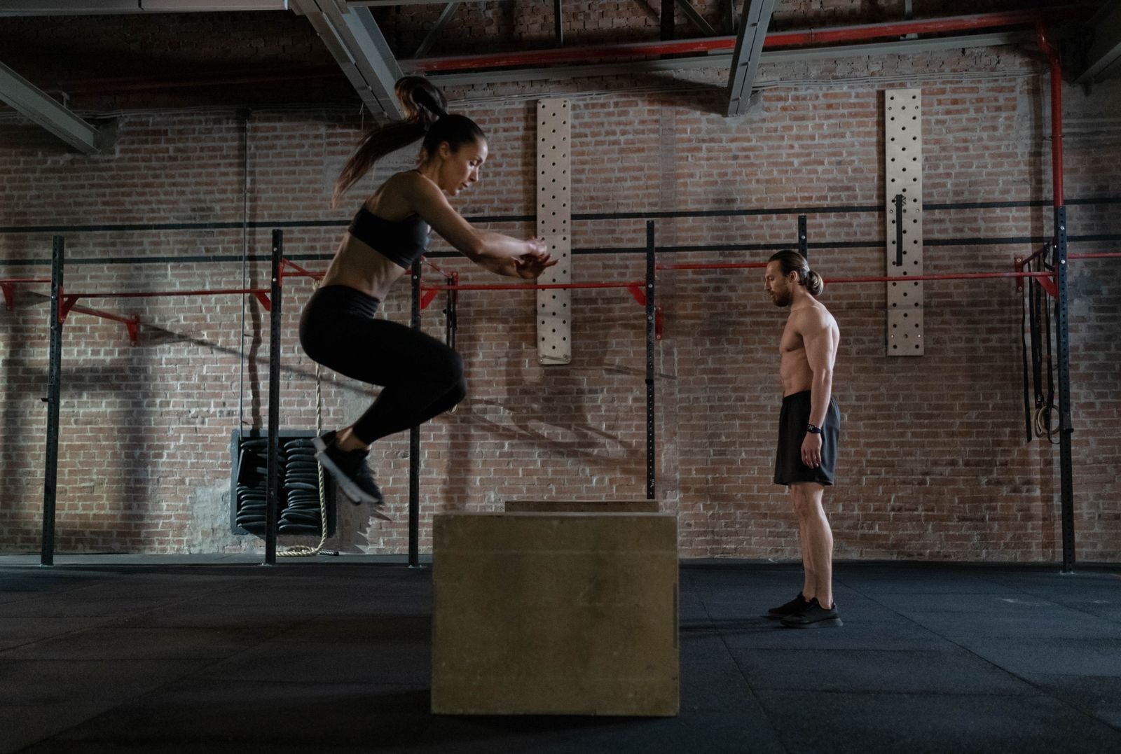 An athlete performing a box jump while a coach watches, the kind of supervised test used in an MCL sprain rehab protocol.