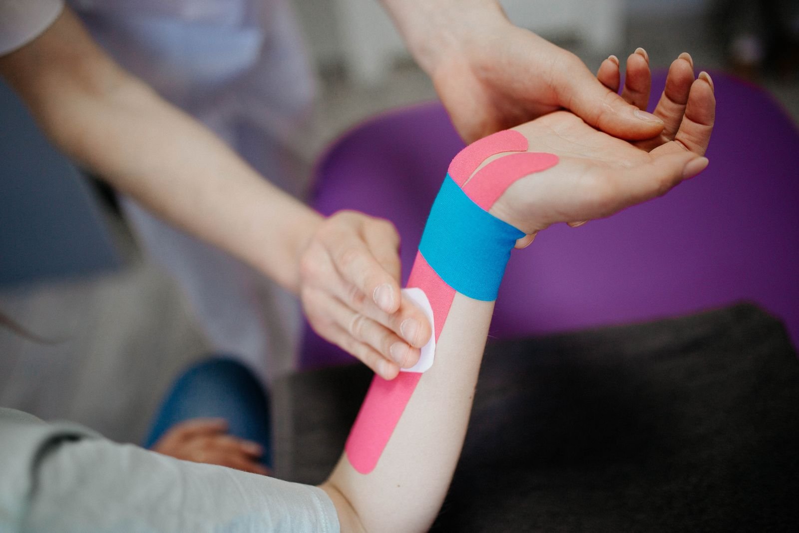 A therapist preparing the skin around a taped wrist, part of good practice for how long to leave kinesiology tape on.